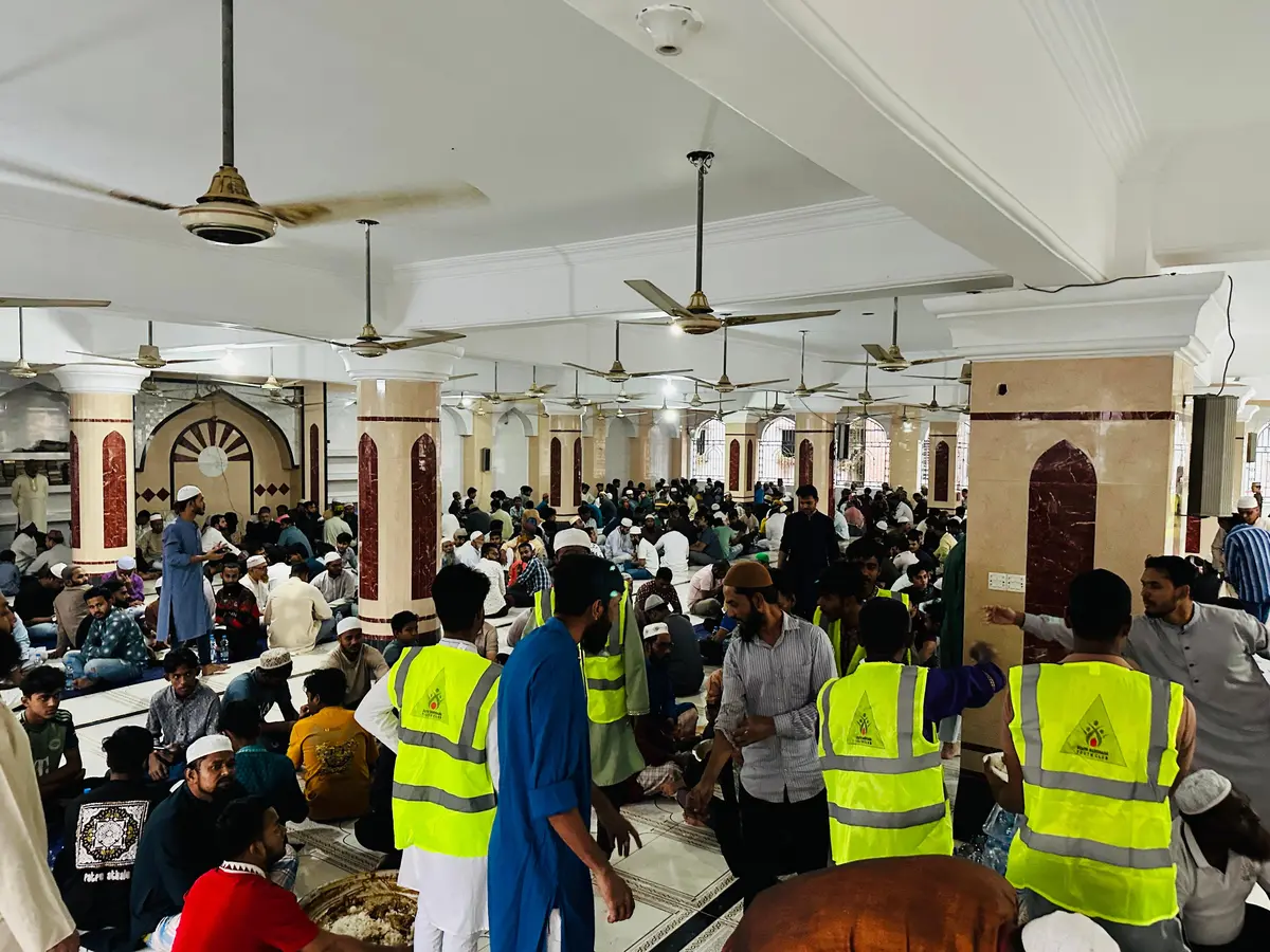 Volunteers coordinating iftar distribution to a packed mosque hall