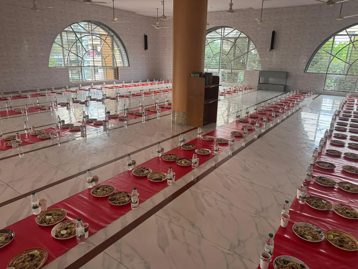 Rows of iftar plates with food and water bottles neatly arranged on red cloth inside the mosque